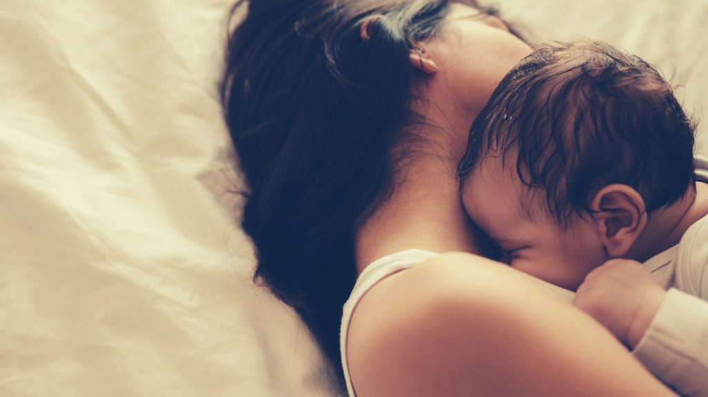 woman with dark hair lying on bed holding baby