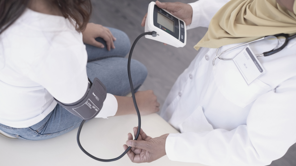 Doctor taking blood pressure of woman in white shirt at 6-week check up