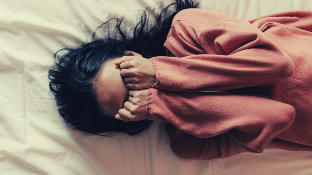 depressed woman with pmad lying on bed covering her eyes with her fists