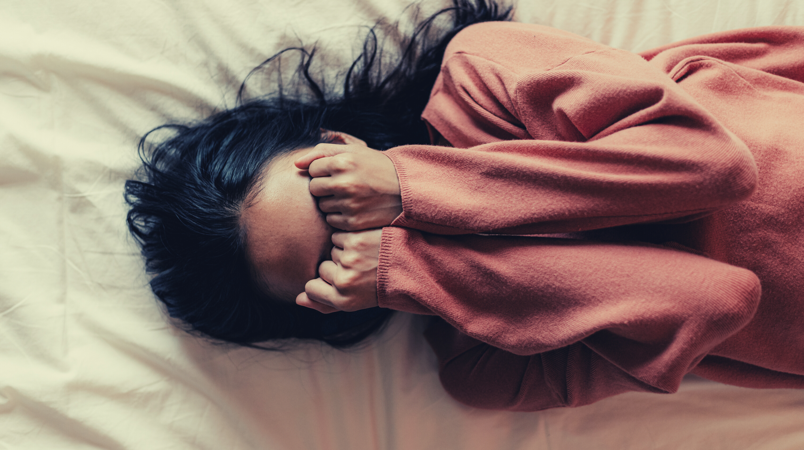 Depressed woman lying on bed covering her eyes with her fists