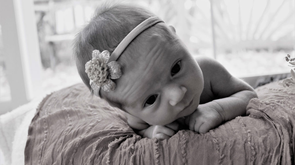 baby with flower headband lying on stomach on pink fabric