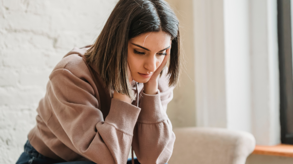 woman with postpartum overwhelm sitting on couch resting head in her hands