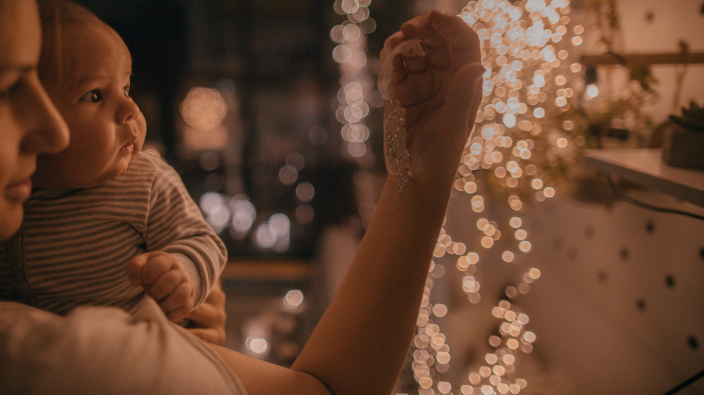 woman with a newborn standing in front of string lights