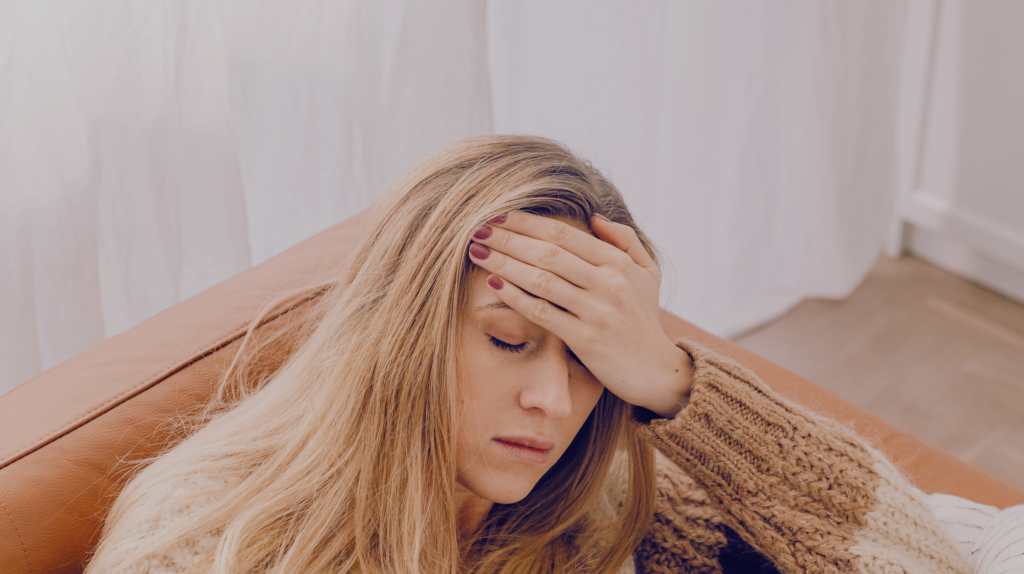 woman sitting on couch with her hand on her forehead, feeling ill, infection