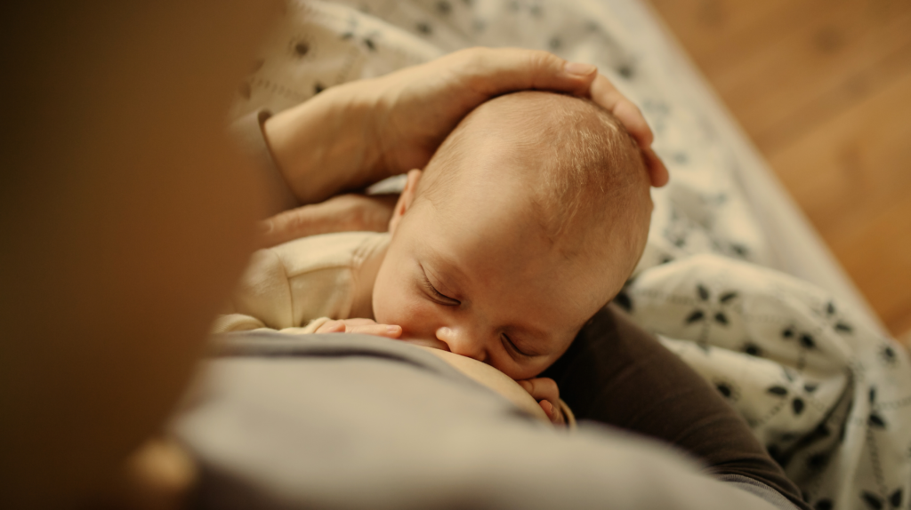 woman sitting in bed holding her breastfeeding newborn