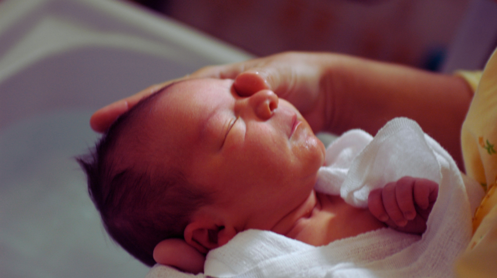 newborn baby swaddled and held in its mother's arms