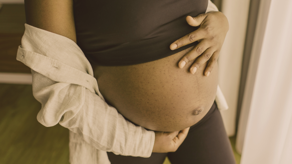 Pregnant woman standing by window with hand touching her bare stomach